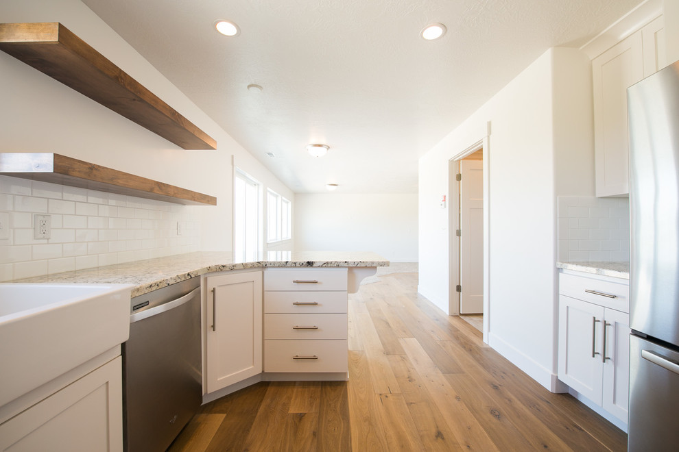 Large arts and crafts eat-in kitchen in Salt Lake City with a farmhouse sink, flat-panel cabinets, white cabinets, granite benchtops, white splashback, subway tile splashback, stainless steel appliances and light hardwood floors.