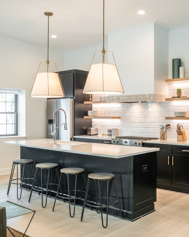 Inspiration for a transitional l-shaped open plan kitchen in Chicago with an undermount sink, shaker cabinets, black cabinets, white splashback, subway tile splashback, stainless steel appliances, light hardwood floors, with island and beige floor.