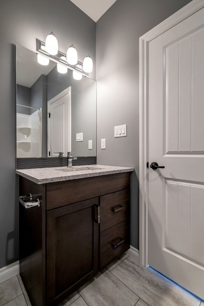This is an example of a large arts and crafts bathroom in Other with shaker cabinets, brown cabinets, an alcove tub, a two-piece toilet, gray tile, ceramic tile, grey walls, ceramic floors, an undermount sink, quartzite benchtops, grey floor, a shower curtain and grey benchtops.
