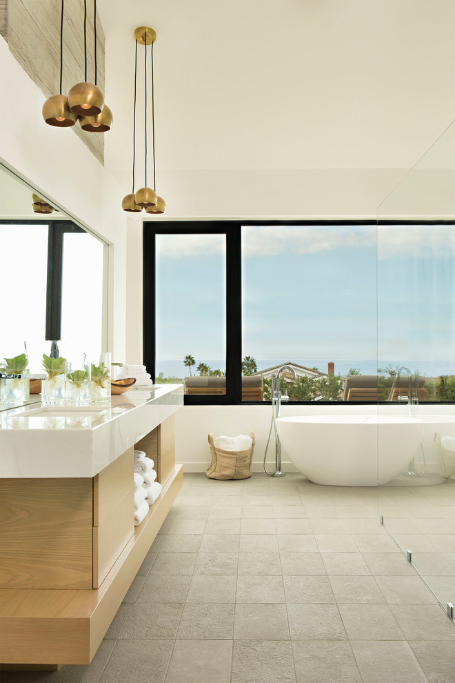 This is an example of a contemporary bathroom in Orange County with flat-panel cabinets, light wood cabinets, a freestanding tub, white tile, white walls and grey floor.
