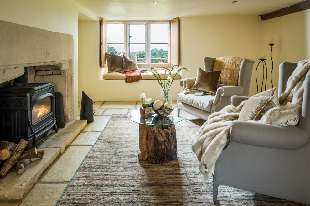 Photo of a mid-sized country formal enclosed living room in Gloucestershire with yellow walls, limestone floors, a wood stove, a stone fireplace surround and beige floor.