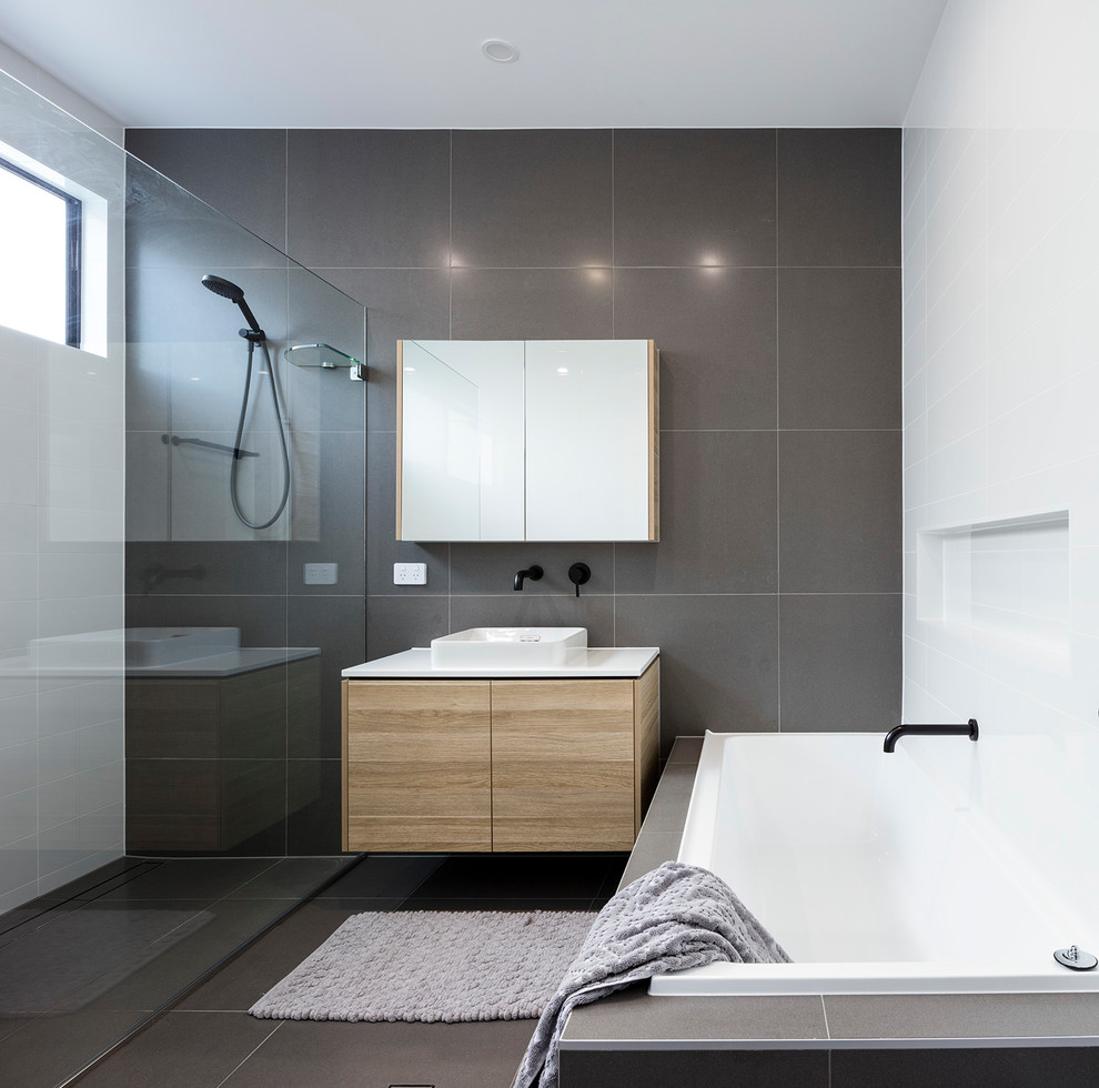 Inspiration for a large contemporary master bathroom in Brisbane with furniture-like cabinets, light wood cabinets, a drop-in tub, an alcove shower, a one-piece toilet, gray tile, porcelain tile, white walls, porcelain floors, a vessel sink, quartzite benchtops, grey floor, a hinged shower door and white benchtops.