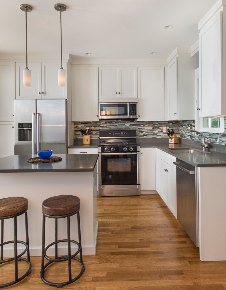 Mid-sized transitional l-shaped medium tone wood floor eat-in kitchen photo in Boston with shaker cabinets, white cabinets, quartz countertops, gray backsplash, glass sheet backsplash, stainless steel appliances, an island and a single-bowl sink