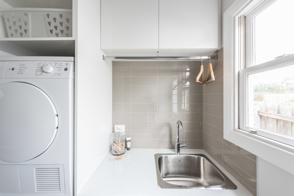 Photo of a small contemporary galley dedicated laundry room in Melbourne with a single-bowl sink, flat-panel cabinets, white cabinets, laminate benchtops, grey walls, medium hardwood floors and a stacked washer and dryer.