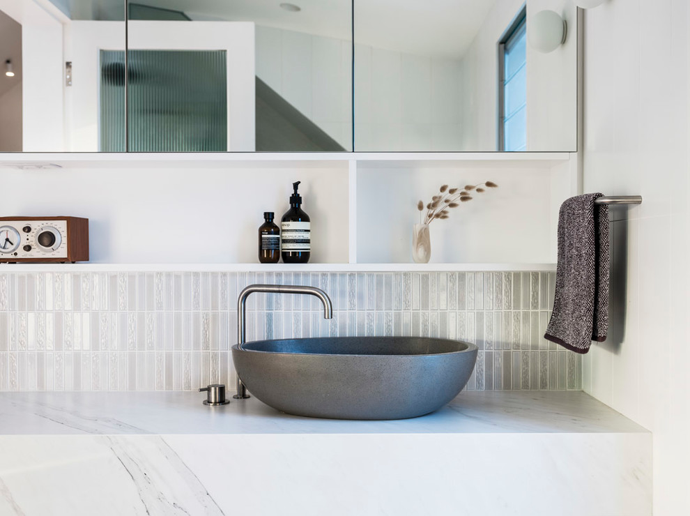 This is an example of a mid-sized contemporary bathroom in Sydney with flat-panel cabinets, white cabinets, a one-piece toilet, white tile, ceramic tile, white walls, ceramic floors, a vessel sink, engineered quartz benchtops, grey floor, a hinged shower door and white benchtops.