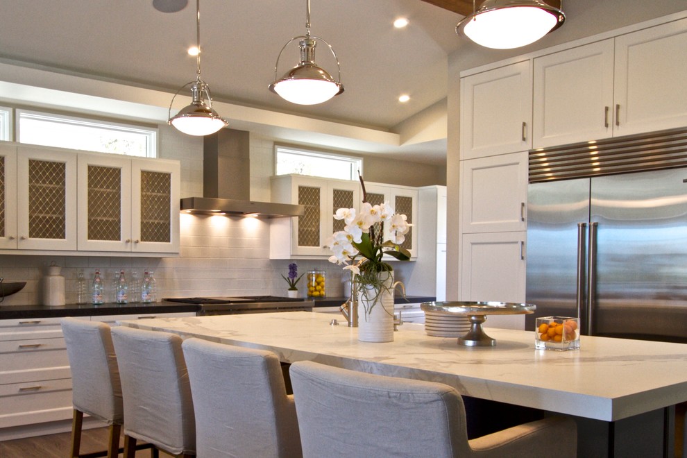 Example of a large transitional single-wall dark wood floor eat-in kitchen design in Orange County with a farmhouse sink, shaker cabinets, white cabinets, marble countertops, white backsplash, subway tile backsplash, stainless steel appliances and an island
