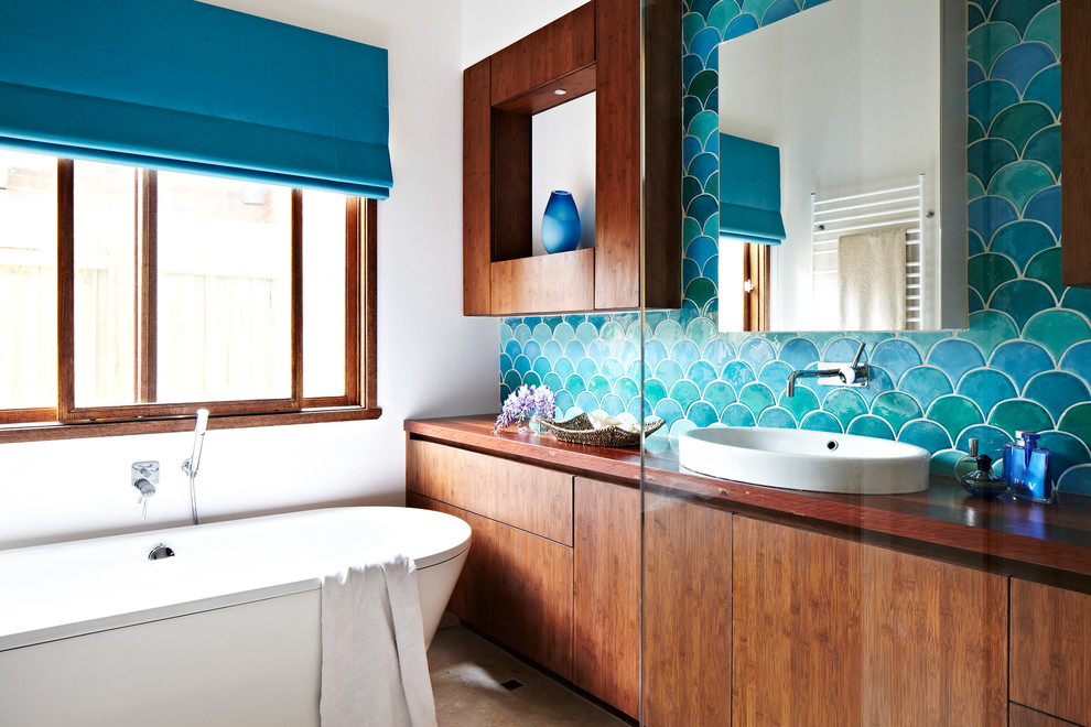 Design ideas for a tropical bathroom in Melbourne with an undermount sink, medium wood cabinets, wood benchtops, a freestanding tub, multi-coloured tile, porcelain tile, white walls and travertine floors.