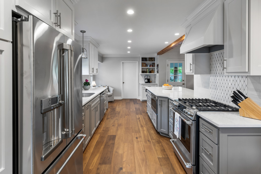 Inspiration for a mid-sized timeless galley medium tone wood floor and brown floor eat-in kitchen remodel in New Orleans with an undermount sink, recessed-panel cabinets, gray cabinets, quartzite countertops, white backsplash, ceramic backsplash, stainless steel appliances, an island and white countertops