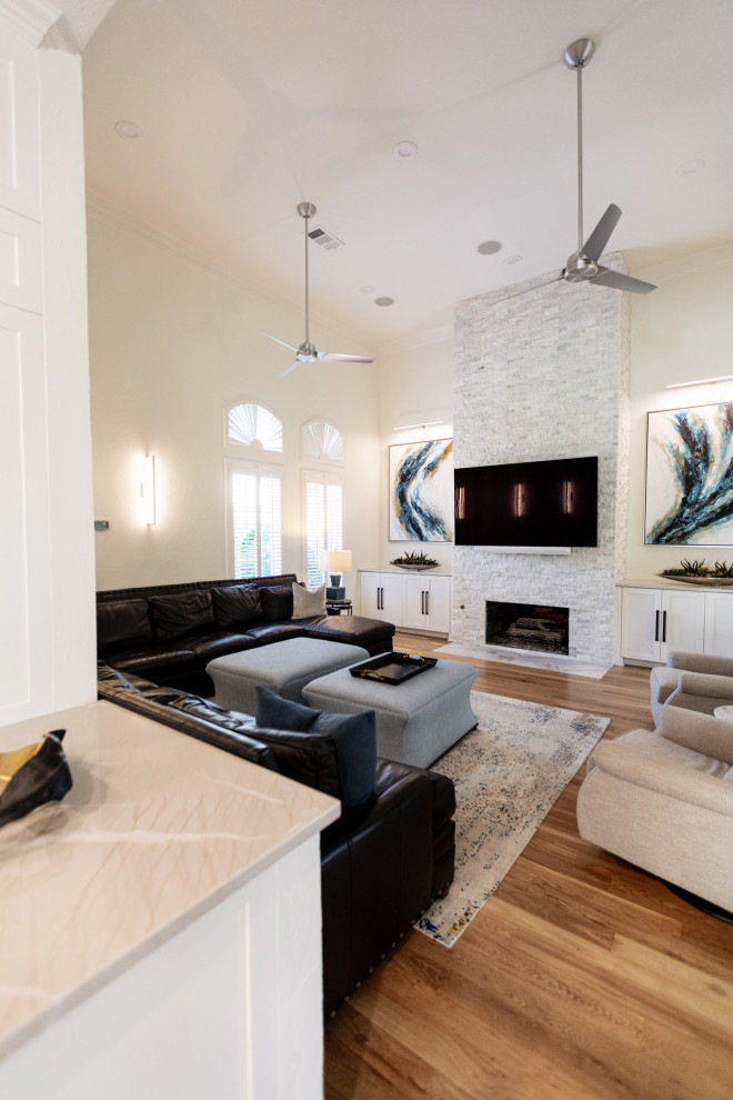 Ejemplo de sala de estar abierta minimalista grande con paredes blancas, suelo de madera clara, todas las chimeneas, piedra de revestimiento, televisor colgado en la pared y suelo marrón