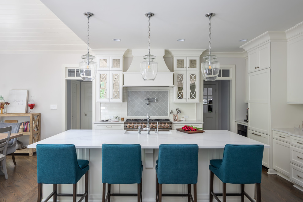 This is an example of a beach style eat-in kitchen in Raleigh with a farmhouse sink, recessed-panel cabinets, white cabinets, grey splashback, stainless steel appliances, dark hardwood floors, with island, brown floor and white benchtop.