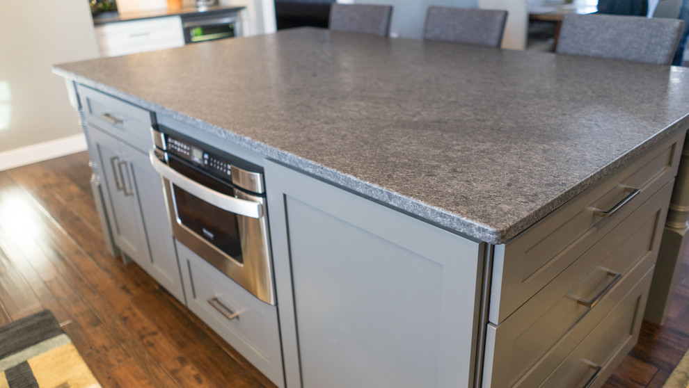 Large transitional u-shaped eat-in kitchen photo with a farmhouse sink, flat-panel cabinets, white cabinets, granite countertops, white backsplash, ceramic backsplash, stainless steel appliances and an island