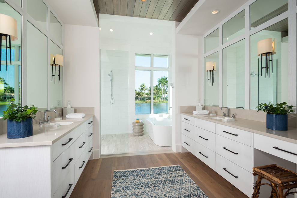 Beach style master wet room bathroom in Miami with flat-panel cabinets, white cabinets, a freestanding tub, white walls, medium hardwood floors, an undermount sink and beige benchtops.
