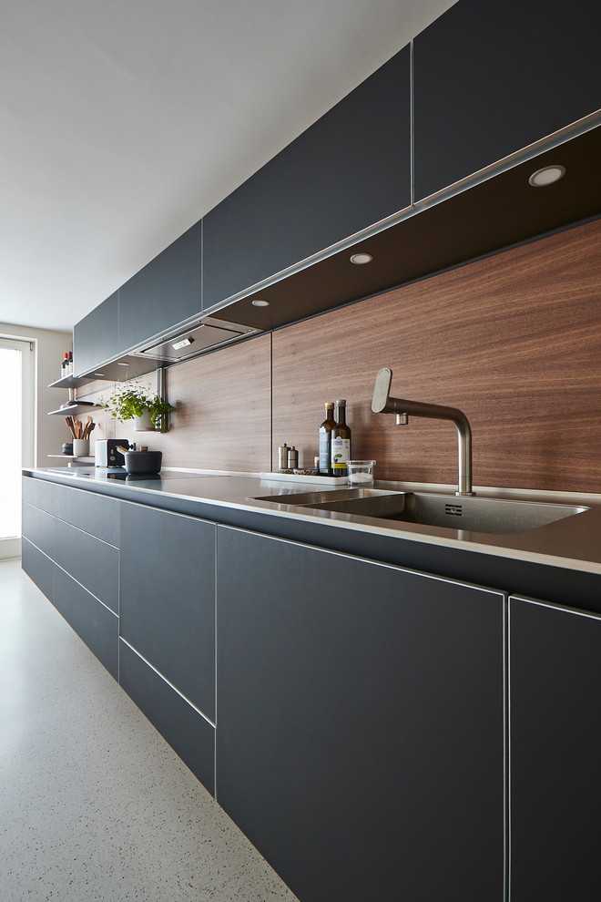 Design ideas for an expansive contemporary single-wall open plan kitchen in Hamburg with an integrated sink, flat-panel cabinets, black cabinets, solid surface benchtops, brown splashback, timber splashback, panelled appliances, linoleum floors, no island, beige floor and white benchtop.