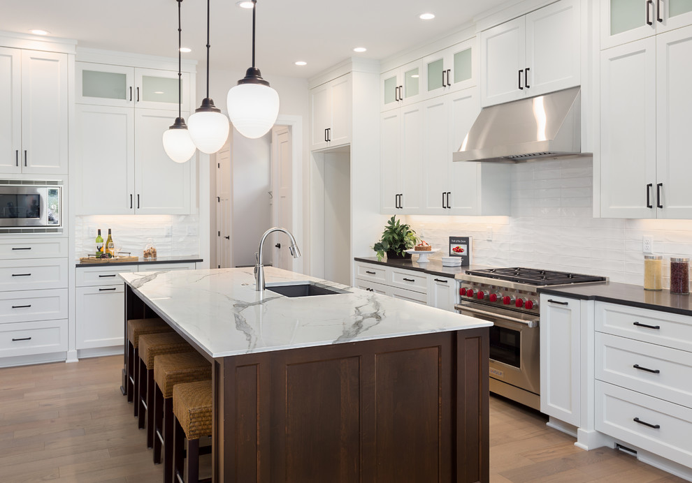 Inspiration for a modern l-shaped open plan kitchen with a drop-in sink, shaker cabinets, white cabinets, tile benchtops, white splashback, subway tile splashback, stainless steel appliances, light hardwood floors, with island, brown floor and white benchtop.