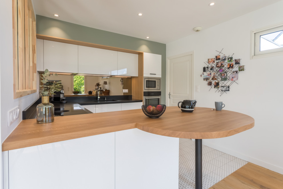 Small modern u-shaped open plan kitchen in Rennes with an integrated sink, flat-panel cabinets, white cabinets, granite worktops, mirror splashback, stainless steel appliances, cement flooring, a breakfast bar, grey floors and black worktops.
