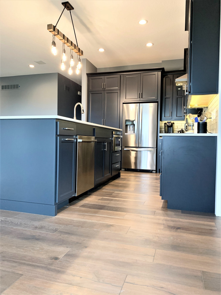 This is an example of a large classic l-shaped open plan kitchen in Other with a submerged sink, flat-panel cabinets, blue cabinets, engineered stone countertops, grey splashback, porcelain splashback, stainless steel appliances, light hardwood flooring, an island, brown floors and white worktops.