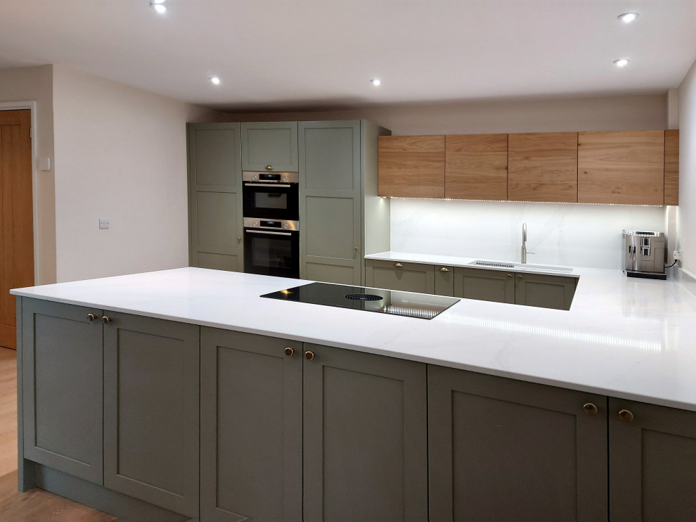 Inspiration for a medium sized traditional u-shaped open plan kitchen in Other with a double-bowl sink, shaker cabinets, green cabinets, quartz worktops, white splashback, engineered quartz splashback, stainless steel appliances, plywood flooring, a breakfast bar, beige floors and white worktops.