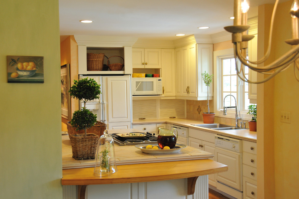 This is an example of a large traditional galley eat-in kitchen in DC Metro with a double-bowl sink, raised-panel cabinets, white cabinets, tile benchtops, grey splashback, ceramic splashback, white appliances and medium hardwood floors.