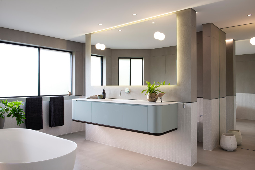 Inspiration for a large contemporary bathroom in Sydney with furniture-like cabinets, blue cabinets, a freestanding tub, an open shower, a one-piece toilet, multi-coloured tile, mosaic tile, multi-coloured walls, porcelain floors, an integrated sink, solid surface benchtops, grey floor, an open shower and white benchtops.