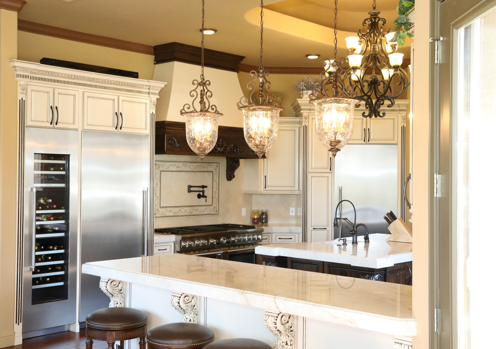 Example of a large tuscan l-shaped dark wood floor and brown floor eat-in kitchen design with a farmhouse sink, raised-panel cabinets, distressed cabinets, quartz countertops, beige backsplash, stone tile backsplash, stainless steel appliances, an island and multicolored countertops