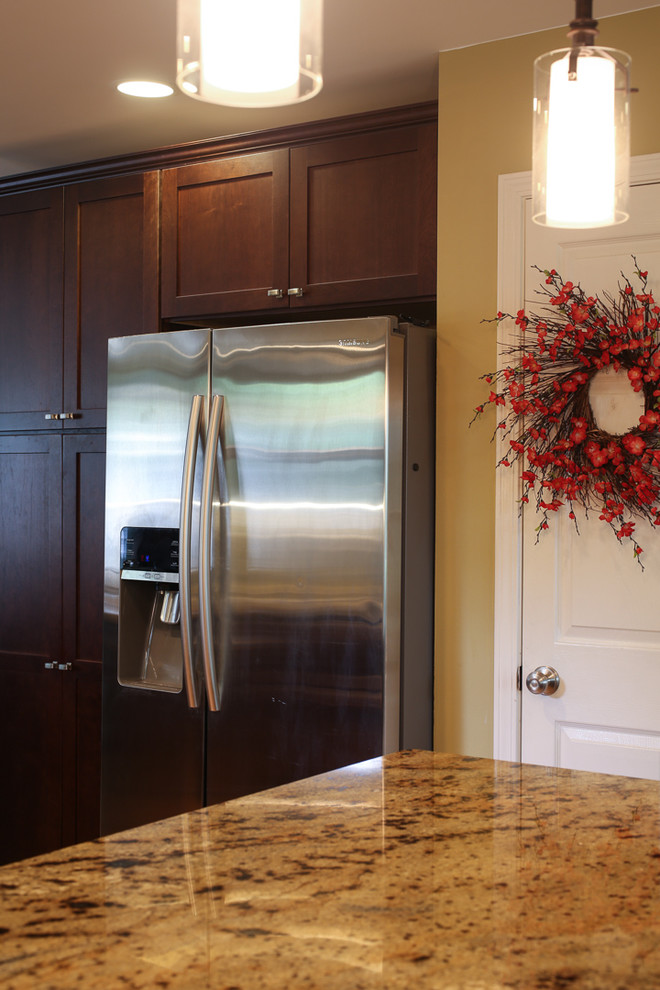 Example of a transitional medium tone wood floor kitchen design with an undermount sink, shaker cabinets, dark wood cabinets, granite countertops, white backsplash, glass tile backsplash and stainless steel appliances