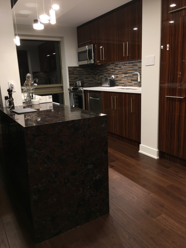This is an example of an expansive modern galley eat-in kitchen in Toronto with an undermount sink, flat-panel cabinets, medium wood cabinets, quartz benchtops, multi-coloured splashback, glass tile splashback, stainless steel appliances, medium hardwood floors, multiple islands, brown floor and black benchtop.