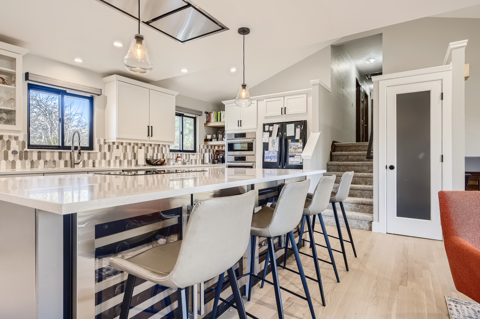 Photo of a contemporary galley open plan kitchen in Denver with an undermount sink, shaker cabinets, white cabinets, quartzite benchtops, grey splashback, ceramic splashback, stainless steel appliances, light hardwood floors, with island and white benchtop.