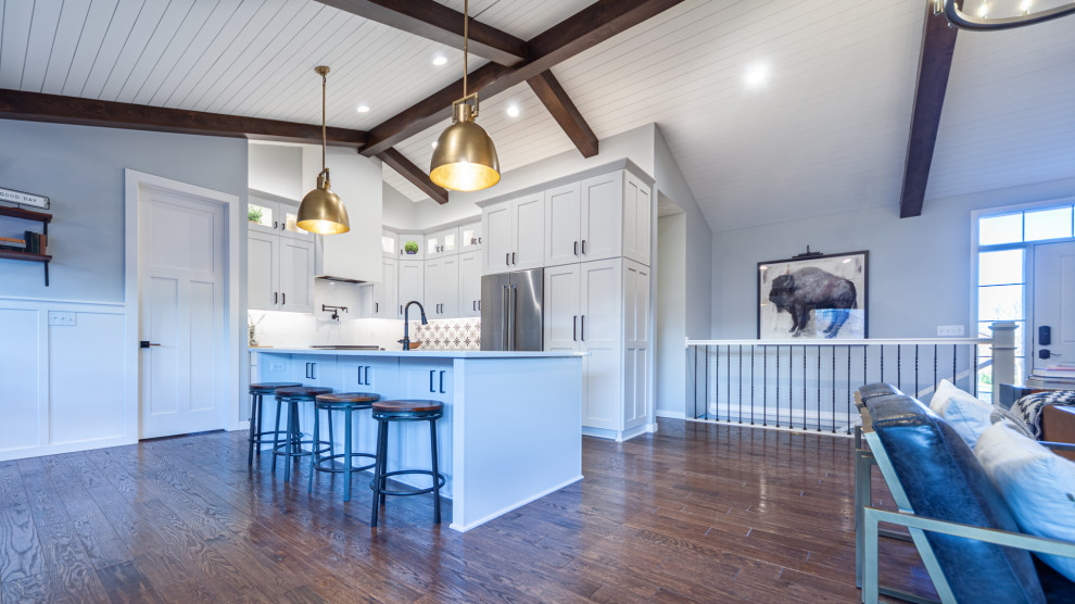Photo of a country l-shaped eat-in kitchen in Other with a farmhouse sink, shaker cabinets, white cabinets, quartz benchtops, white splashback, engineered quartz splashback, stainless steel appliances, medium hardwood floors, with island, white benchtop and timber.