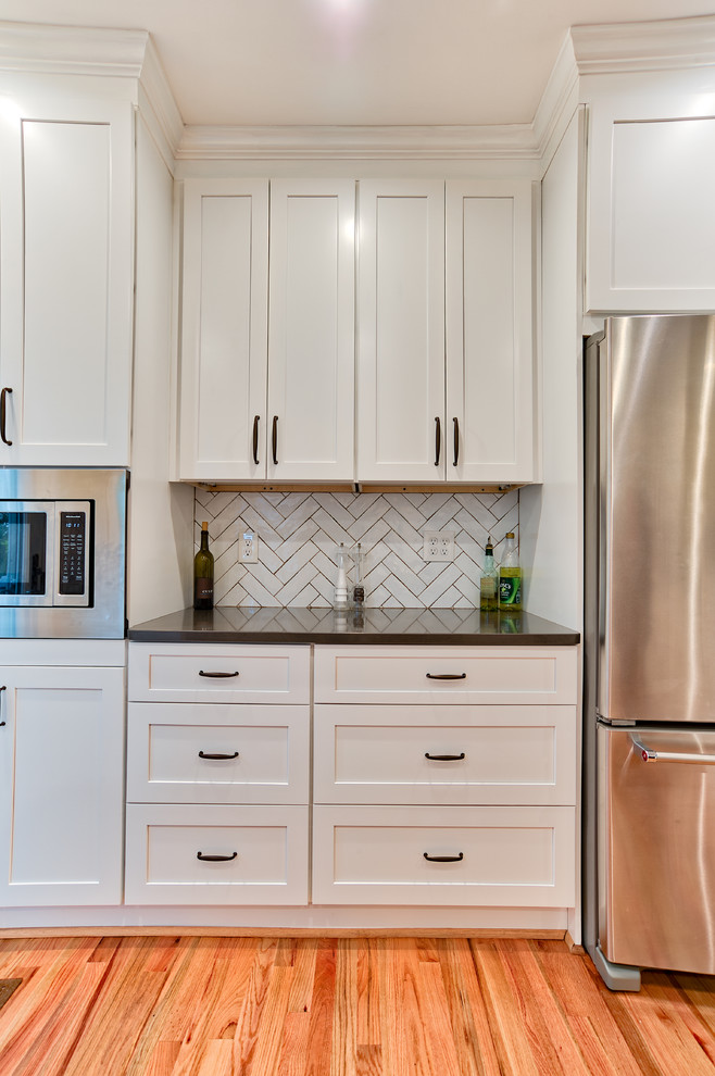 Mid-sized transitional u-shaped eat-in kitchen in Philadelphia with shaker cabinets, white cabinets, glass benchtops, white splashback, subway tile splashback, light hardwood floors, a peninsula, multi-coloured floor, brown benchtop, an undermount sink and stainless steel appliances.