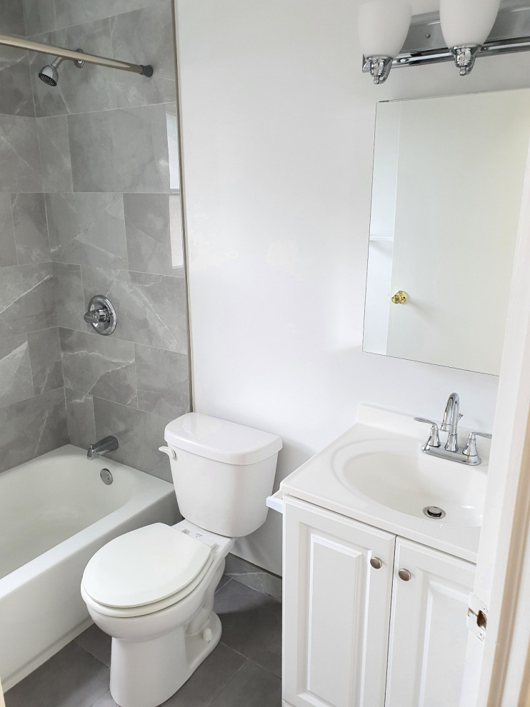 ニューヨークにある低価格の中くらいなトラディショナルスタイルのおしゃれな浴室 (レイズドパネル扉のキャビネット、白いキャビネット、コーナー型浴槽、シャワー付き浴槽	、分離型トイレ、グレーのタイル、セラミックタイル、白い壁、セラミックタイルの床、一体型シンク、クオーツストーンの洗面台、グレーの床、シャワーカーテン、白い洗面カウンター、洗面台1つ、独立型洗面台) の写真
