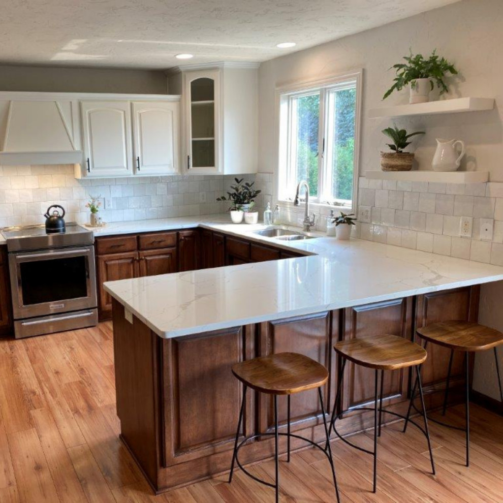 This is an example of a small transitional u-shaped eat-in kitchen in Minneapolis with an undermount sink, raised-panel cabinets, medium wood cabinets, quartz benchtops, white splashback, cement tile splashback, stainless steel appliances, medium hardwood floors, a peninsula, brown floor and white benchtop.
