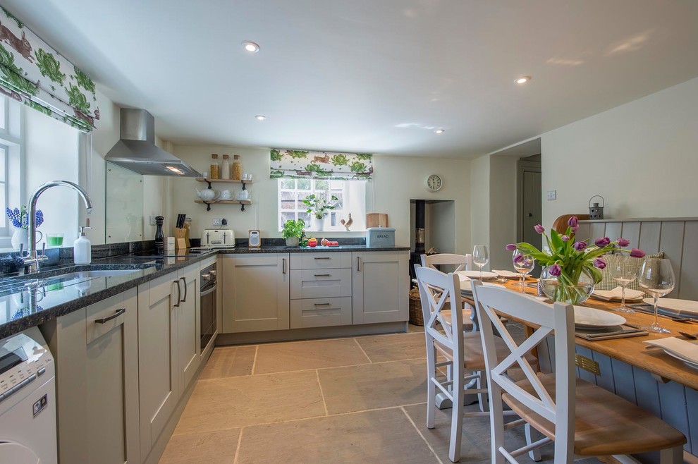 This is an example of a mid-sized country eat-in kitchen in Other with an undermount sink, shaker cabinets, grey cabinets, granite benchtops, blue splashback, glass sheet splashback, stainless steel appliances and grey floor.