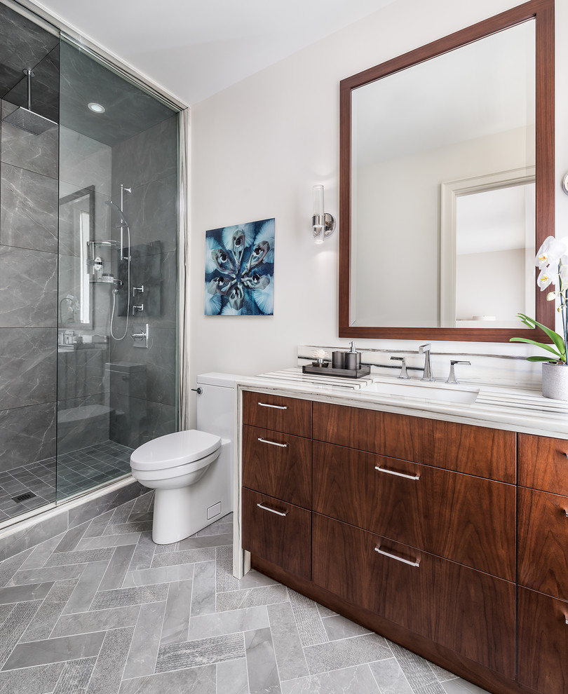 Mid-sized transitional bathroom in Toronto with flat-panel cabinets, medium wood cabinets, an alcove shower, a one-piece toilet, gray tile, ceramic tile, grey walls, ceramic floors, an undermount sink, marble benchtops, grey floor and a hinged shower door.