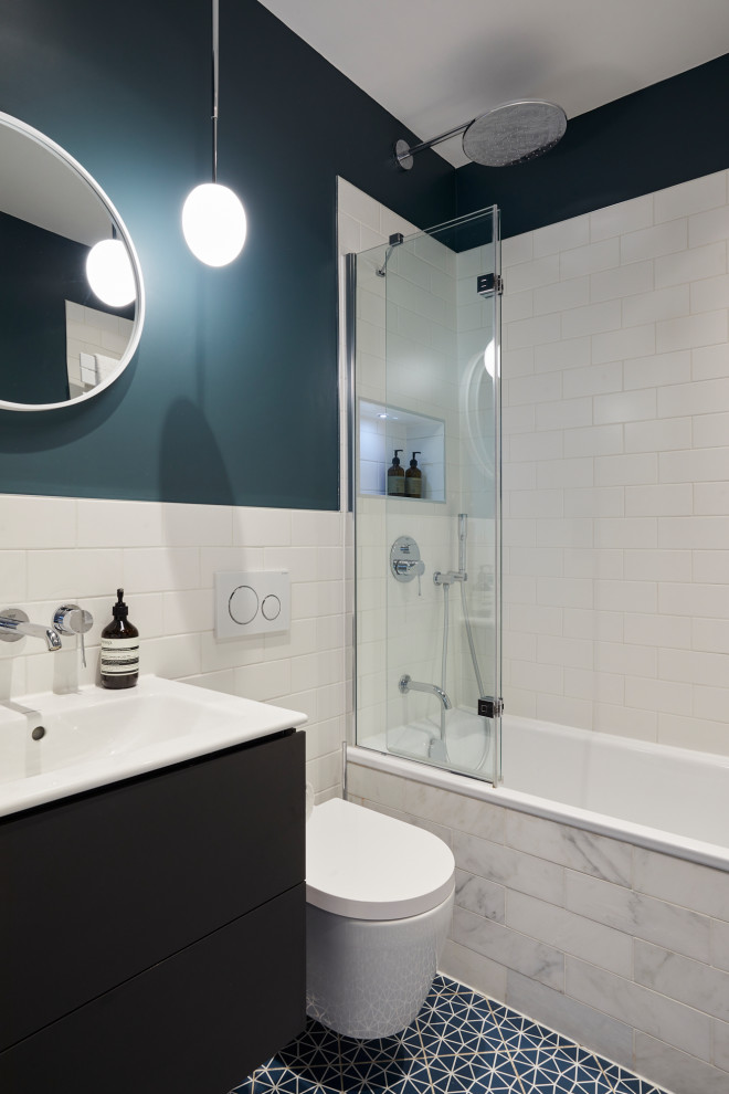 Photo of a medium sized modern family bathroom in London with flat-panel cabinets, brown cabinets, an alcove bath, a shower/bath combination, a wall mounted toilet, white tiles, porcelain tiles, blue walls, porcelain flooring, an integrated sink, blue floors, a hinged door, a single sink, a floating vanity unit and a feature wall.