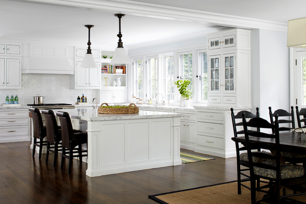 This is an example of a mid-sized traditional l-shaped eat-in kitchen in New York with white cabinets, white splashback, subway tile splashback, stainless steel appliances, dark hardwood floors, with island and beaded inset cabinets.
