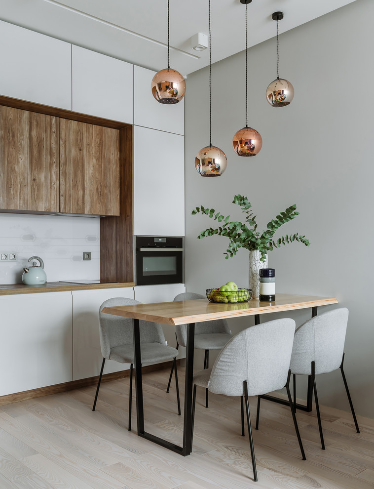 This is an example of a contemporary single-wall eat-in kitchen in Moscow with flat-panel cabinets, white cabinets, wood benchtops, white splashback, black appliances, light hardwood floors, no island and beige floor.