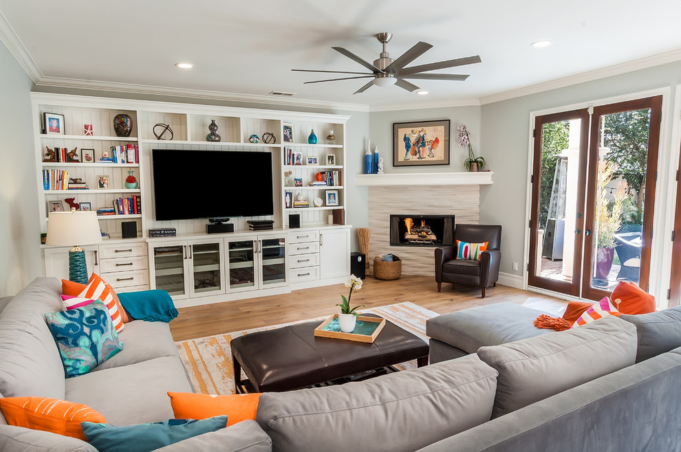 This is an example of a large beach style open concept family room in Los Angeles with grey walls, light hardwood floors, a corner fireplace, a stone fireplace surround, a wall-mounted tv and multi-coloured floor.