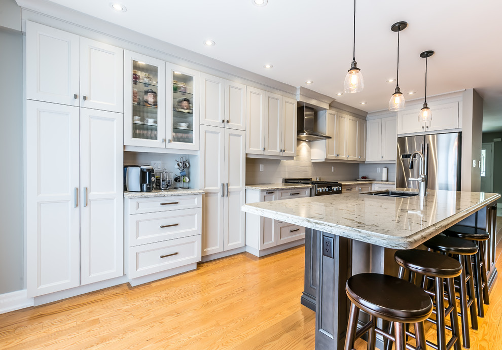 Kitchen - mid-sized transitional l-shaped brown floor kitchen idea in Toronto with a double-bowl sink, white cabinets, white backsplash, stainless steel appliances and an island