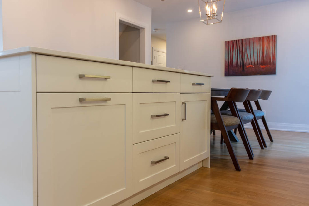 Example of a large transitional l-shaped light wood floor eat-in kitchen design in Ottawa with a farmhouse sink, shaker cabinets, white cabinets, quartz countertops, white backsplash, porcelain backsplash, stainless steel appliances, an island and white countertops