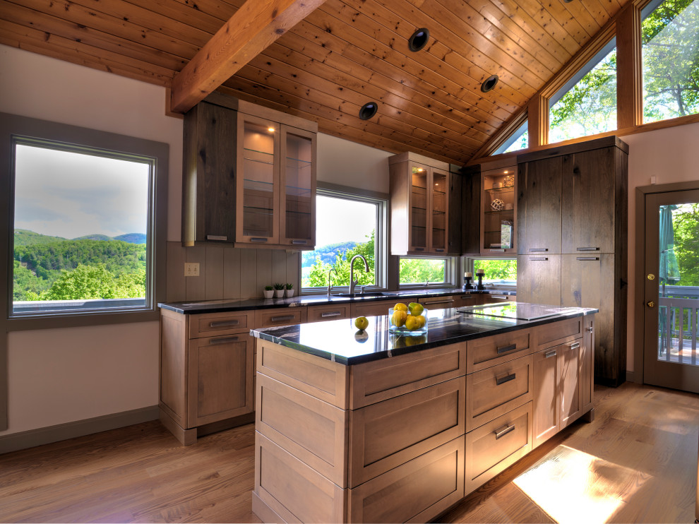 Mid-sized country u-shaped eat-in kitchen in Other with a single-bowl sink, glass-front cabinets, distressed cabinets, granite benchtops, beige splashback, timber splashback, stainless steel appliances, light hardwood floors, with island, brown floor, black benchtop and vaulted.