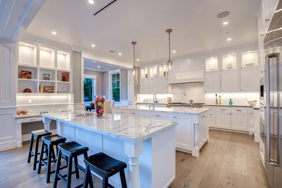 Design ideas for a traditional u-shaped kitchen in Los Angeles with a farmhouse sink, shaker cabinets, white cabinets, white splashback, stainless steel appliances, dark hardwood floors and with island.
