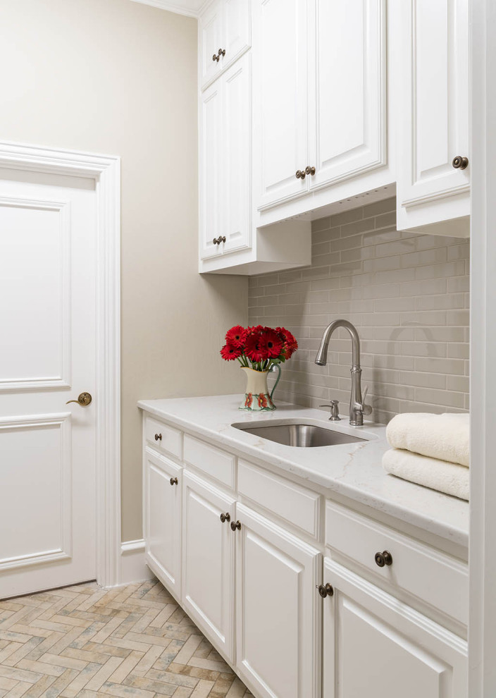 This is an example of a traditional galley dedicated laundry room in Dallas with white cabinets, grey splashback, beige walls, beige floor and white benchtop.