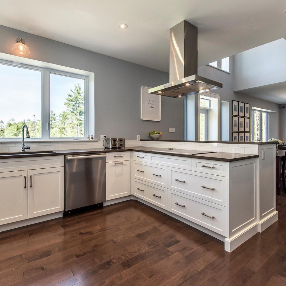 Example of a mid-sized u-shaped medium tone wood floor and brown floor kitchen design with an undermount sink, recessed-panel cabinets, white cabinets, quartzite countertops, white backsplash, subway tile backsplash, stainless steel appliances, no island and black countertops