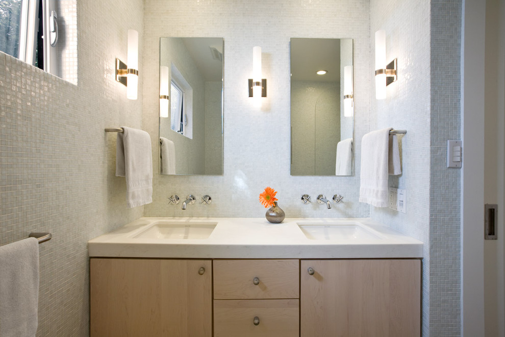 This is an example of a mid-sized contemporary bathroom in San Francisco with flat-panel cabinets, light wood cabinets, white tile, engineered quartz benchtops, a corner tub, a two-piece toilet, white walls, marble floors and an undermount sink.