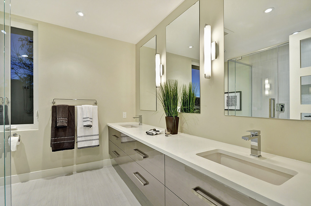 This is an example of a large contemporary master bathroom in Ottawa with flat-panel cabinets, beige cabinets, gray tile, porcelain tile, solid surface benchtops, white benchtops, an alcove shower, beige walls, laminate floors, an undermount sink, grey floor and a hinged shower door.