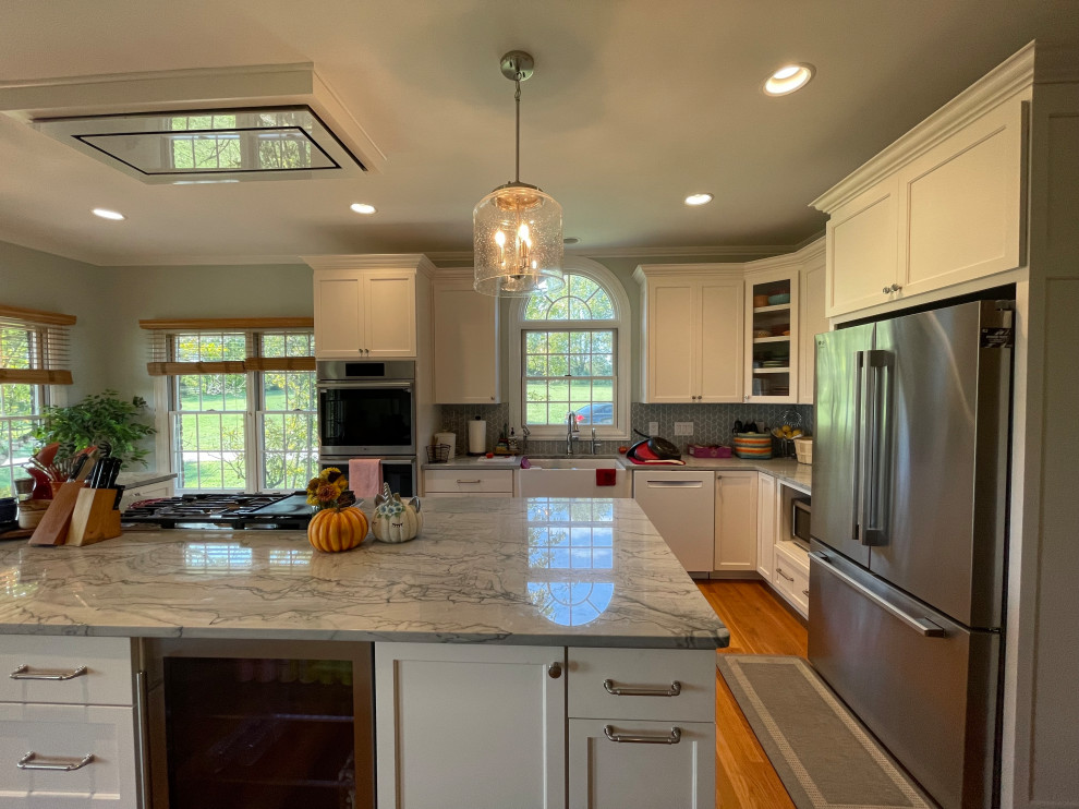 Large transitional light wood floor and brown floor eat-in kitchen photo with an undermount sink, shaker cabinets, white cabinets, quartzite countertops, green backsplash, marble backsplash, stainless steel appliances, an island and gray countertops