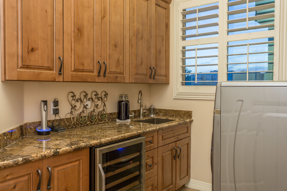 This is an example of a small country galley dedicated laundry room in Phoenix with a drop-in sink, recessed-panel cabinets, medium wood cabinets, granite benchtops, beige walls, terra-cotta floors and a side-by-side washer and dryer.