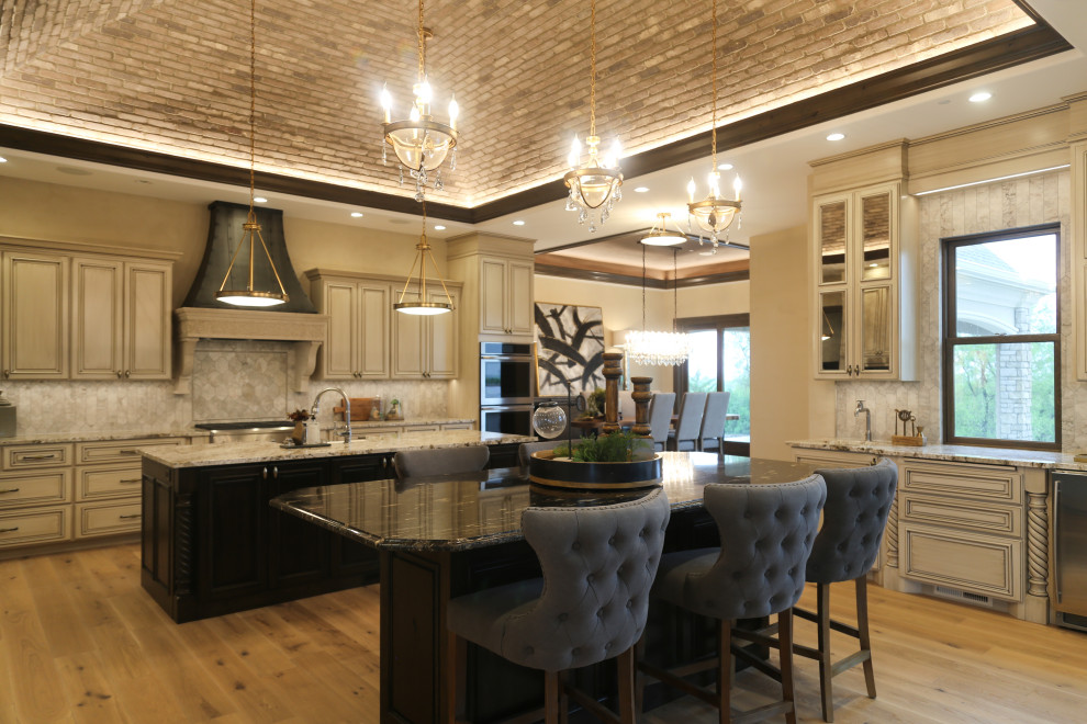 Photo of a large u-shaped eat-in kitchen in Other with a farmhouse sink, beaded inset cabinets, beige cabinets, granite benchtops, beige splashback, porcelain splashback, stainless steel appliances, medium hardwood floors, multiple islands, brown floor, multi-coloured benchtop and vaulted.