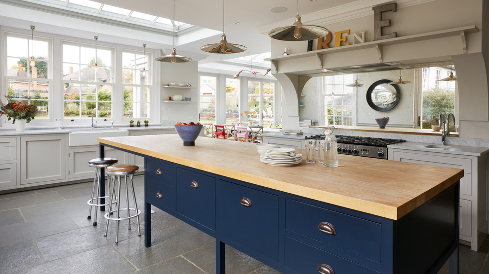 This is an example of a large transitional open plan kitchen in Essex with a farmhouse sink, recessed-panel cabinets, grey cabinets, marble benchtops, mirror splashback, stainless steel appliances, with island, grey floor and grey benchtop.