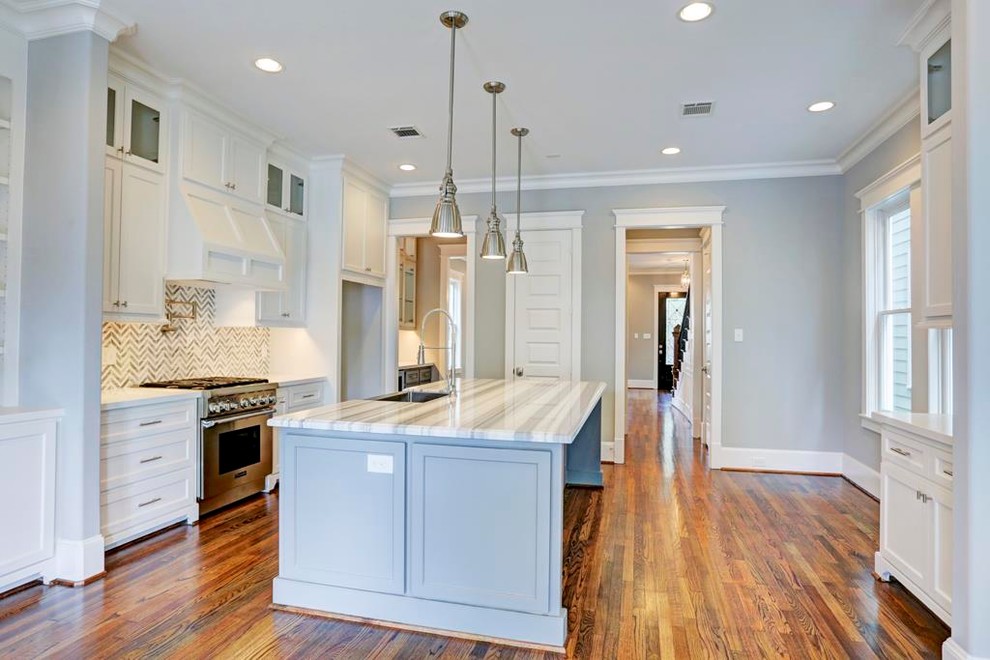 Design ideas for a mid-sized traditional galley eat-in kitchen in Houston with a double-bowl sink, recessed-panel cabinets, white cabinets, marble benchtops, grey splashback, stone tile splashback, stainless steel appliances, light hardwood floors, with island and brown floor.